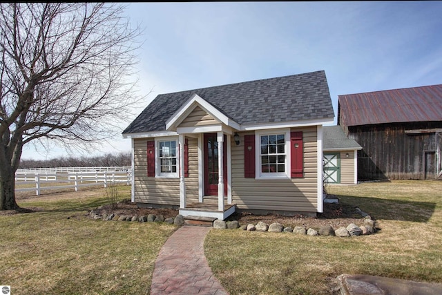 bungalow with roof with shingles, an outdoor structure, fence, and a front lawn