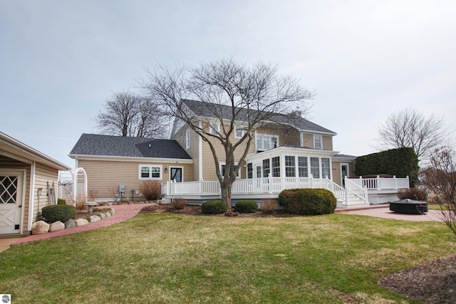 back of property with a sunroom, a yard, a wooden deck, and a fire pit