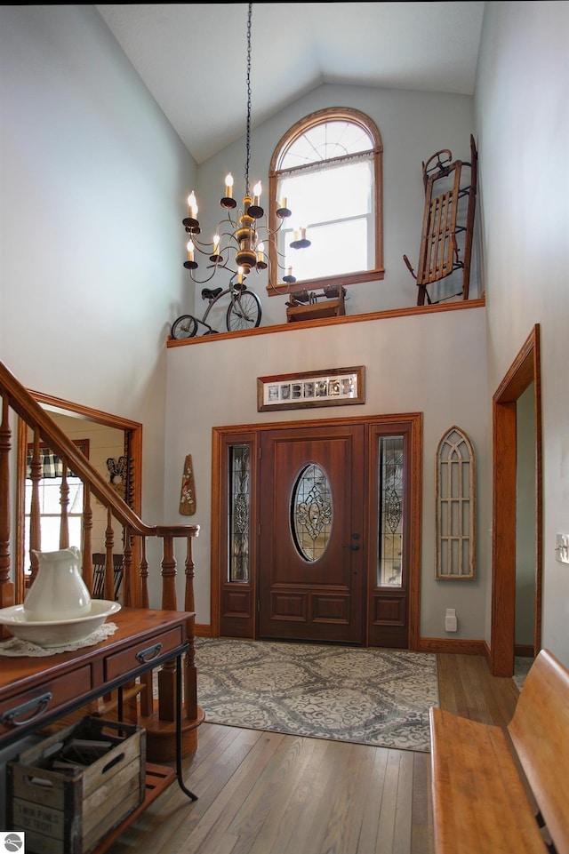 entrance foyer featuring wood-type flooring, high vaulted ceiling, a notable chandelier, and stairs