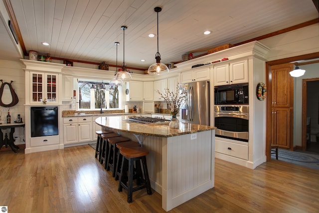 kitchen with stainless steel appliances, dark stone countertops, light wood-style flooring, and a kitchen island