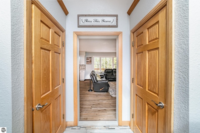 hallway with light wood-style flooring, a textured wall, and baseboards