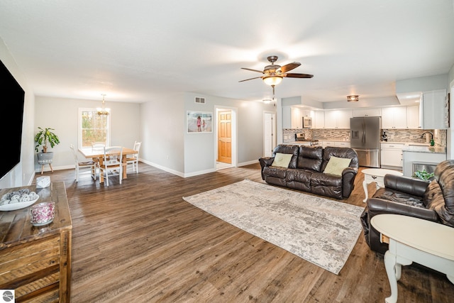 living room featuring ceiling fan with notable chandelier, wood finished floors, baseboards, and visible vents