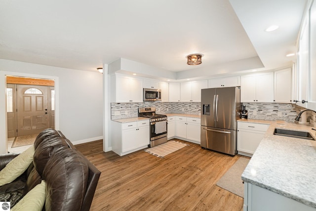 kitchen featuring baseboards, light wood-type flooring, decorative backsplash, stainless steel appliances, and a sink
