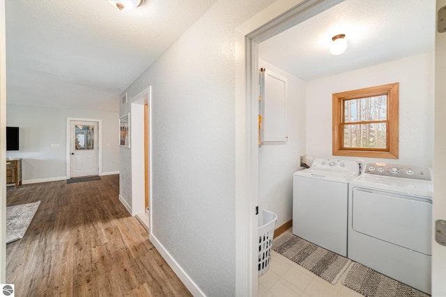 clothes washing area with washer and clothes dryer, a healthy amount of sunlight, laundry area, and wood finished floors