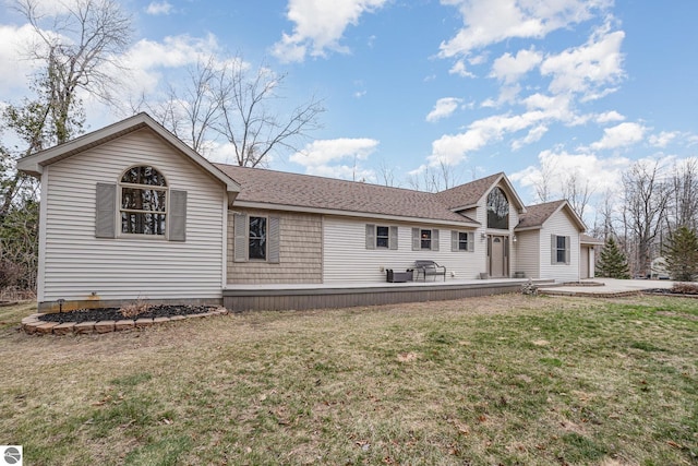 rear view of property with a shingled roof, a deck, and a lawn