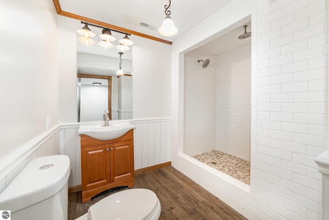 bathroom with a tile shower, visible vents, a wainscoted wall, toilet, and wood finished floors
