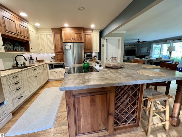 kitchen with ceiling fan, light wood-style flooring, a center island, a sink, and stainless steel appliances