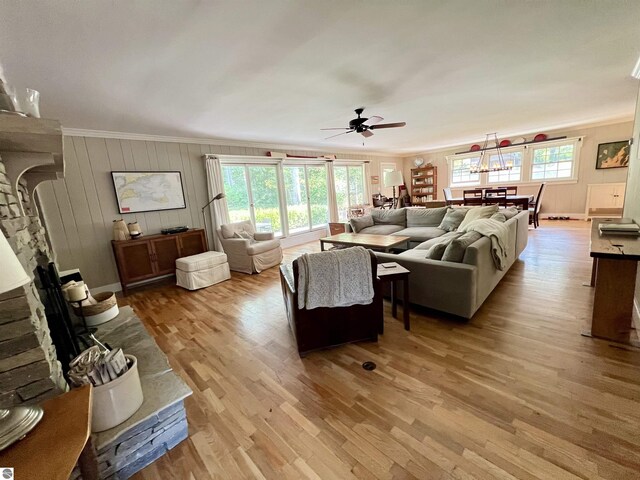 living room featuring a ceiling fan, crown molding, wood finished floors, and a fireplace with raised hearth