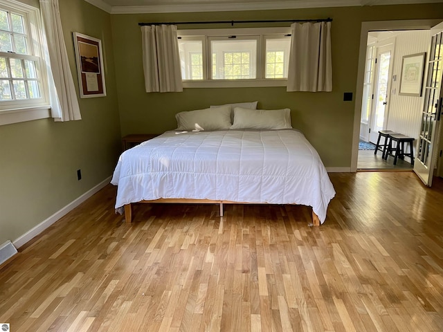 bedroom featuring light wood-type flooring, crown molding, and baseboards
