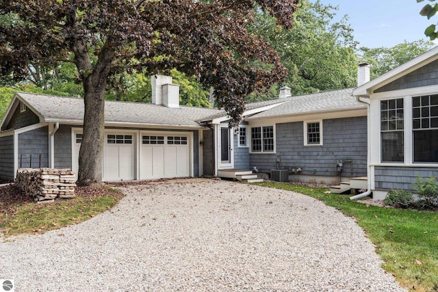 single story home with central air condition unit, roof with shingles, gravel driveway, an attached garage, and a chimney