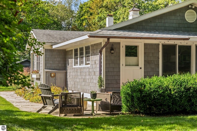 exterior space featuring a patio area, a shingled roof, a lawn, and a chimney