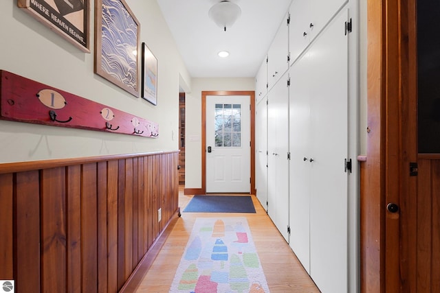 doorway to outside with wooden walls, light wood finished floors, and wainscoting