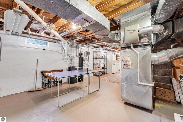 below grade area featuring water heater, concrete block wall, and freestanding refrigerator
