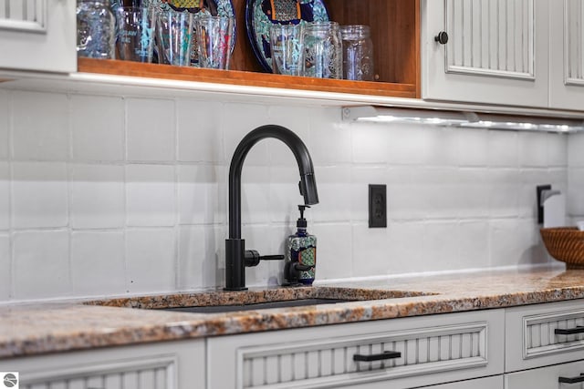 room details with tasteful backsplash, stone countertops, a sink, and white cabinetry