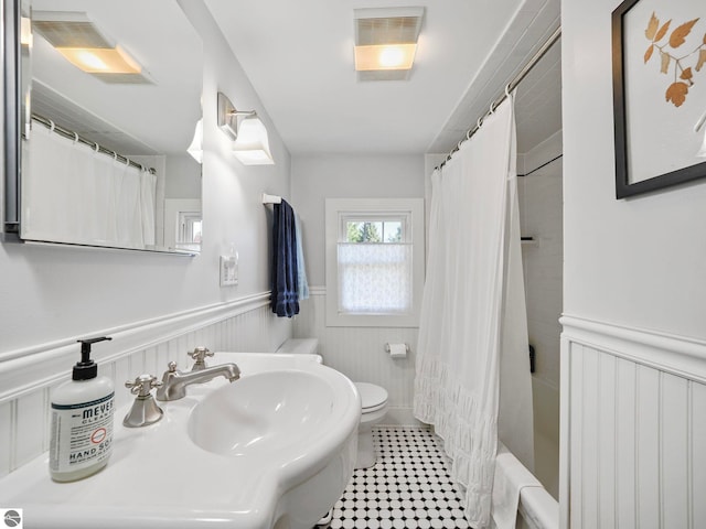 bathroom featuring shower / bath combination with curtain, toilet, wainscoting, visible vents, and a sink