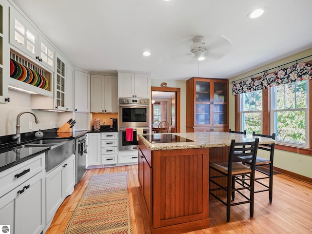 kitchen with ceiling fan, light wood-type flooring, a center island, a sink, and stainless steel appliances