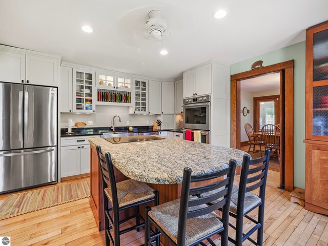 kitchen featuring appliances with stainless steel finishes, white cabinetry, light wood-style flooring, a kitchen island, and a breakfast bar area