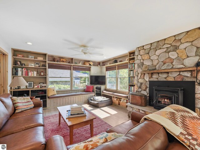 living area featuring a stone fireplace, wood finished floors, and ceiling fan