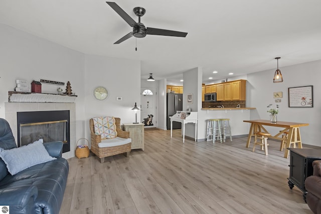 living area featuring light wood-type flooring, a tiled fireplace, a ceiling fan, and recessed lighting