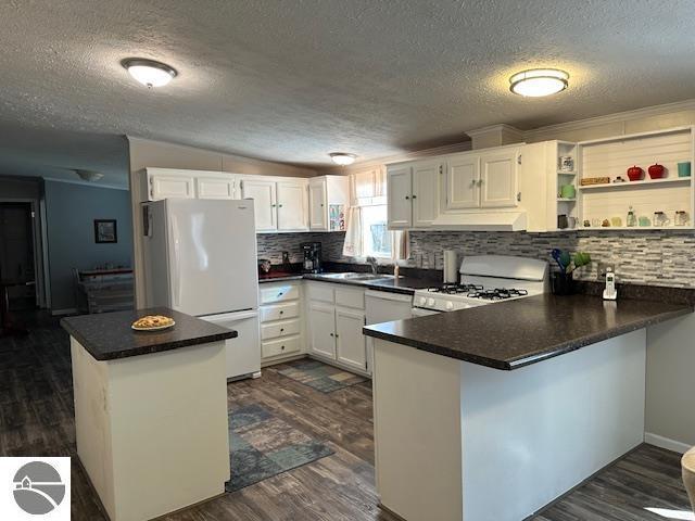 kitchen featuring a peninsula, backsplash, a textured ceiling, and white appliances
