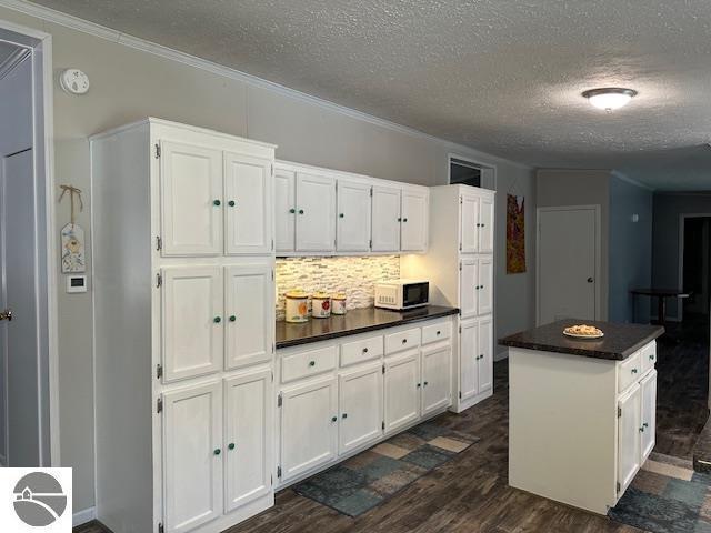 kitchen with white cabinetry, dark wood-style flooring, dark countertops, and white microwave