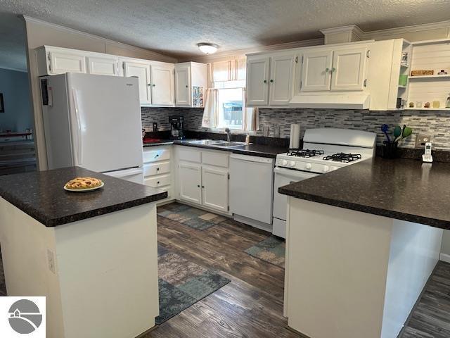 kitchen featuring under cabinet range hood, white appliances, a textured ceiling, and backsplash