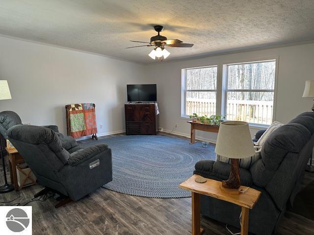 living room with a ceiling fan, baseboards, a textured ceiling, and dark wood finished floors
