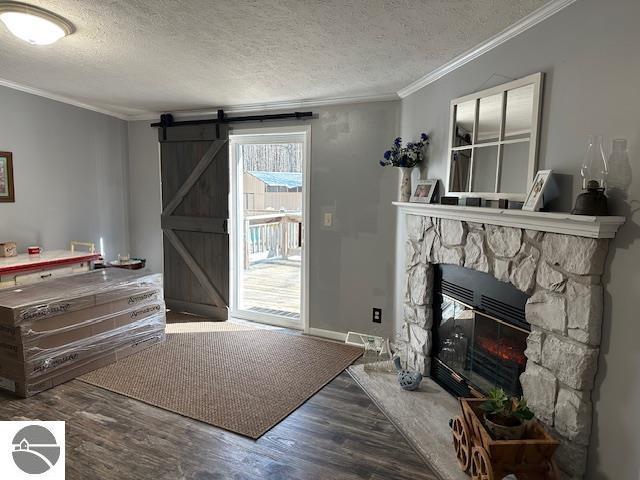 living area with a barn door, a stone fireplace, wood finished floors, a textured ceiling, and ornamental molding