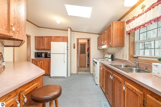 kitchen featuring vaulted ceiling with skylight, a sink, ornamental molding, white appliances, and wallpapered walls
