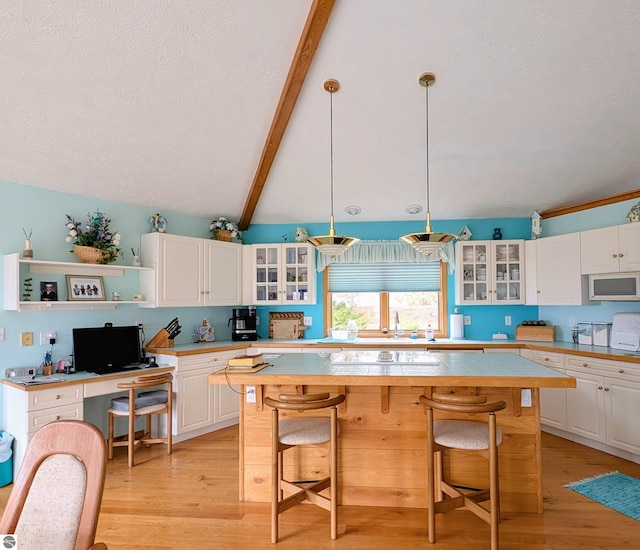 kitchen featuring light countertops, white microwave, white cabinetry, and a breakfast bar