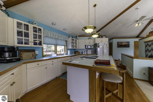 kitchen featuring freestanding refrigerator, dark wood finished floors, vaulted ceiling, stainless steel microwave, and a sink