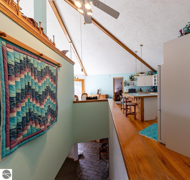 hallway featuring light wood-type flooring, a textured ceiling, and vaulted ceiling with beams