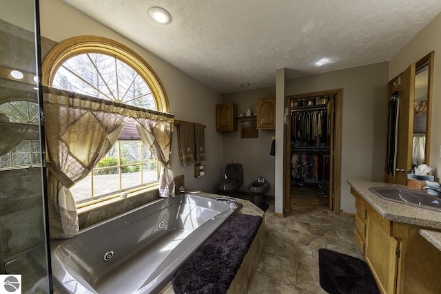 bathroom featuring a textured ceiling, stone tile floors, vanity, a tub with jets, and toilet