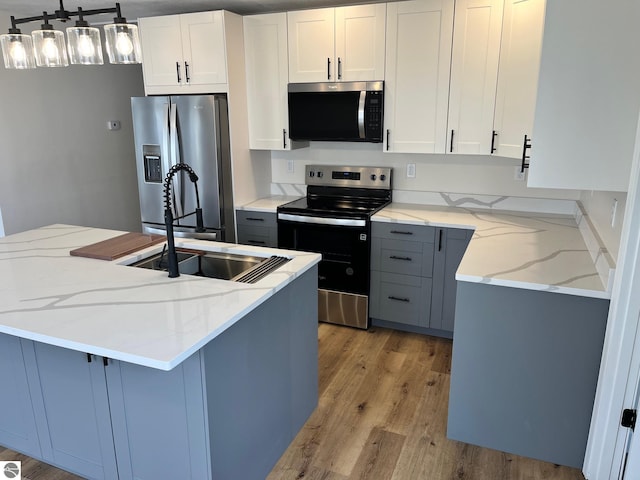kitchen featuring white cabinetry, light stone counters, stainless steel appliances, and light wood finished floors