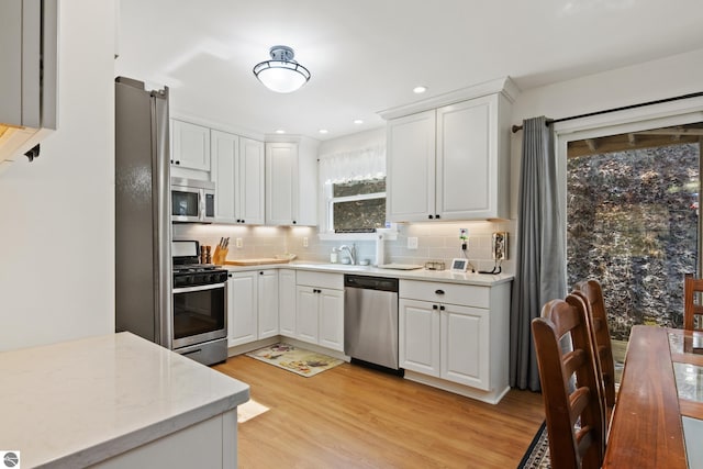 kitchen featuring white cabinetry, appliances with stainless steel finishes, a sink, light wood finished floors, and decorative backsplash