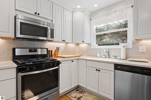 kitchen featuring tasteful backsplash, white cabinets, a sink, light countertops, and appliances with stainless steel finishes