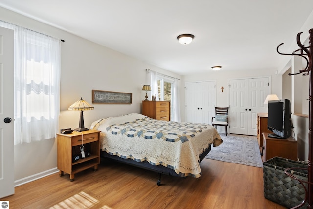 bedroom featuring multiple closets, wood finished floors, and baseboards
