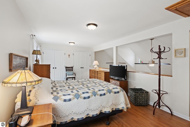 bedroom with baseboards, two closets, and wood finished floors