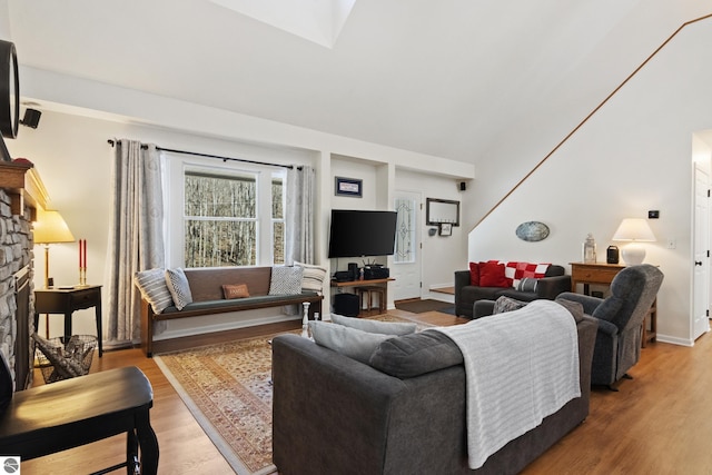 living room with a fireplace, a towering ceiling, a skylight, and wood finished floors