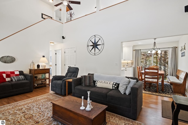 living room featuring a high ceiling, wood finished floors, and ceiling fan with notable chandelier