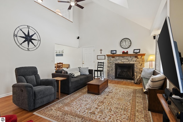 living area featuring baseboards, ceiling fan, a fireplace, wood finished floors, and high vaulted ceiling