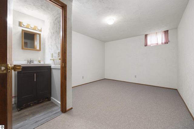 basement featuring light carpet, baseboards, a sink, and a textured ceiling