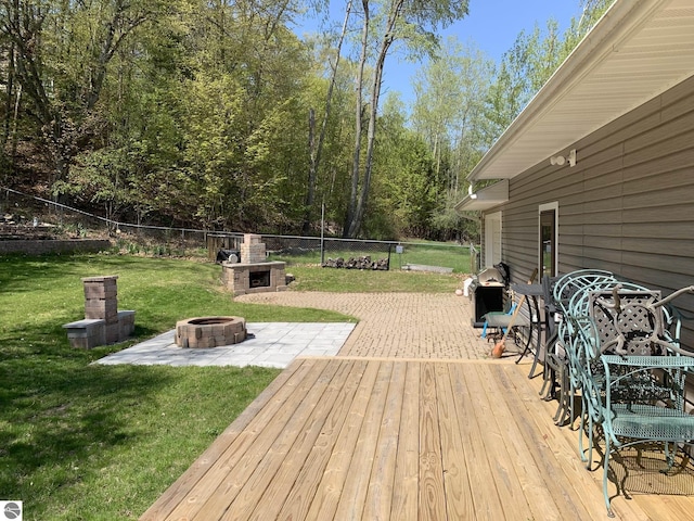 wooden terrace with a patio, exterior fireplace, a fire pit, fence, and a lawn