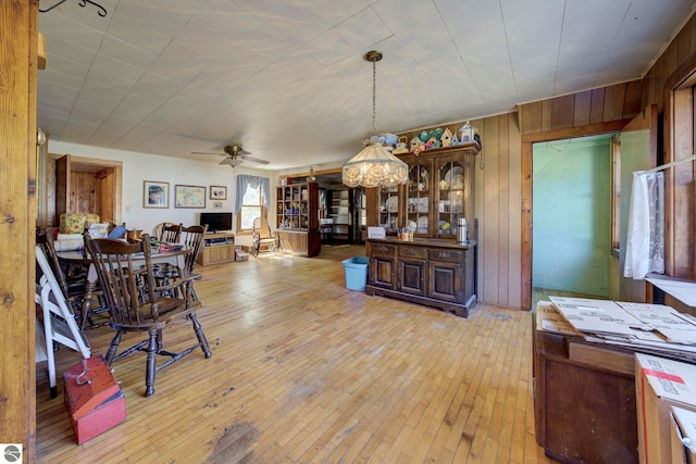 dining area featuring light wood-type flooring, wood walls, and a ceiling fan