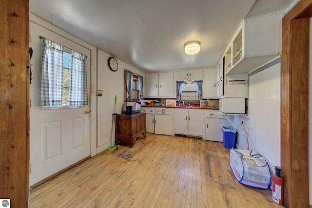 kitchen with white microwave, light wood finished floors, white cabinetry, and a wealth of natural light