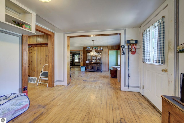 foyer entrance with wooden walls, visible vents, and light wood-type flooring