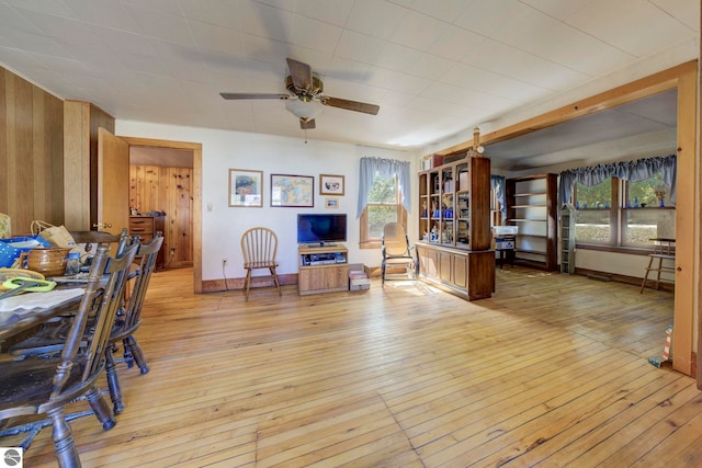 living area with wood walls, baseboards, light wood finished floors, and a ceiling fan
