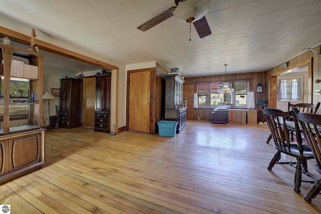 living room with wood walls, light wood-style floors, and a ceiling fan