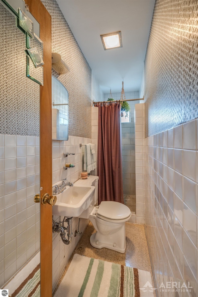 full bathroom featuring a sink, a tile shower, toilet, and tile walls