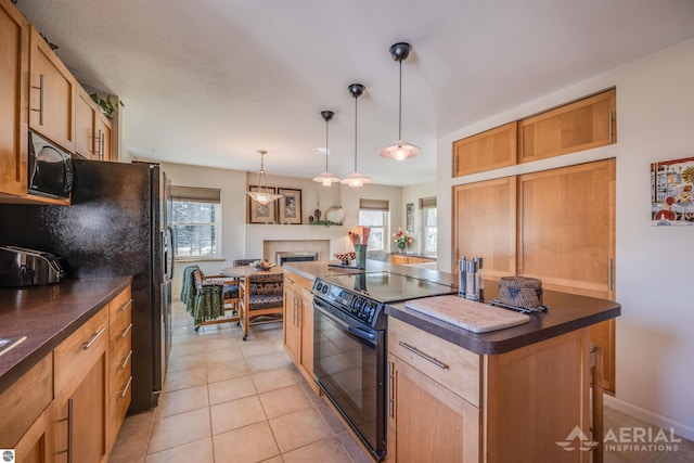 kitchen featuring a tile fireplace, decorative light fixtures, a kitchen island, black appliances, and dark countertops